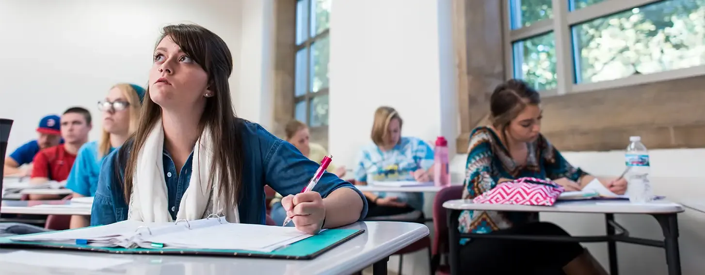 Students taking notes sitting at desks in a classroom setting.