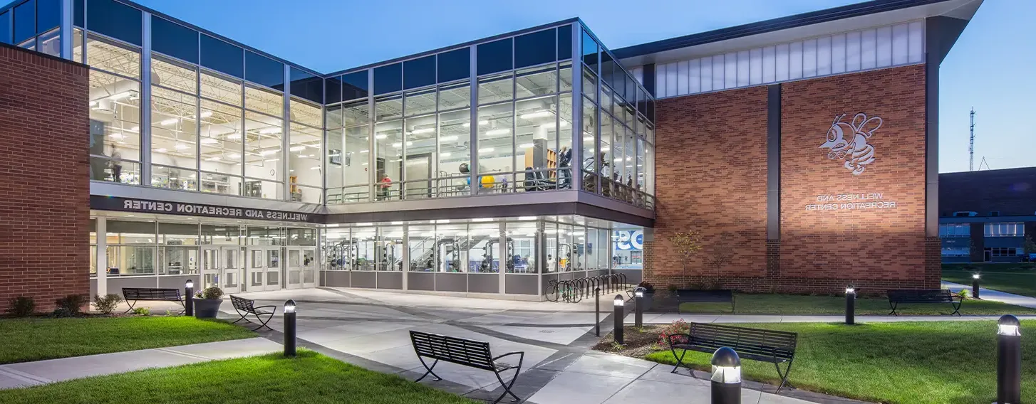 The St. Ambrose Wellness and Recreation Center at dusk featuring multiple people exercising inside.